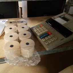 Rollen toiletpapier in kunststofverpakking naast een kasregister op een werkblad
