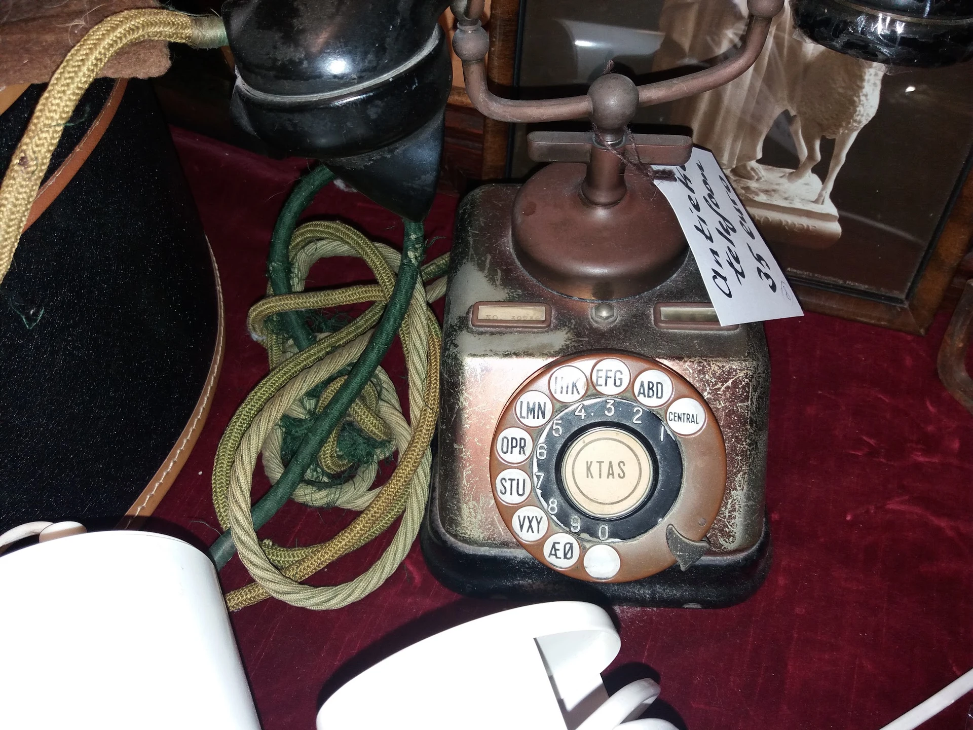 Antieke telefoon met draaischijf en metalen behuizing op rode doek, omgeven door kabels