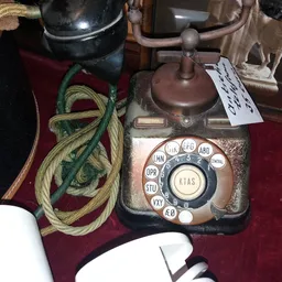 Antieke telefoon met draaischijf en metalen behuizing op rode doek, omgeven door kabels