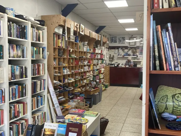 Winkelinterieur met boekenrekken langs de wanden en centrale houten boekenkasten vol met tweedehands boeken