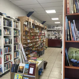 Kringloopwinkel met boekenkasten, houten stellingen met boeken en diverse artikelen, toonbank op achtergrond