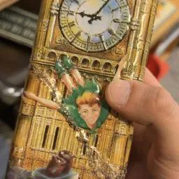 Close-up van een goudkleurig vintage voorwerp met een Peter Pan-afbeelding en klokwerk erop