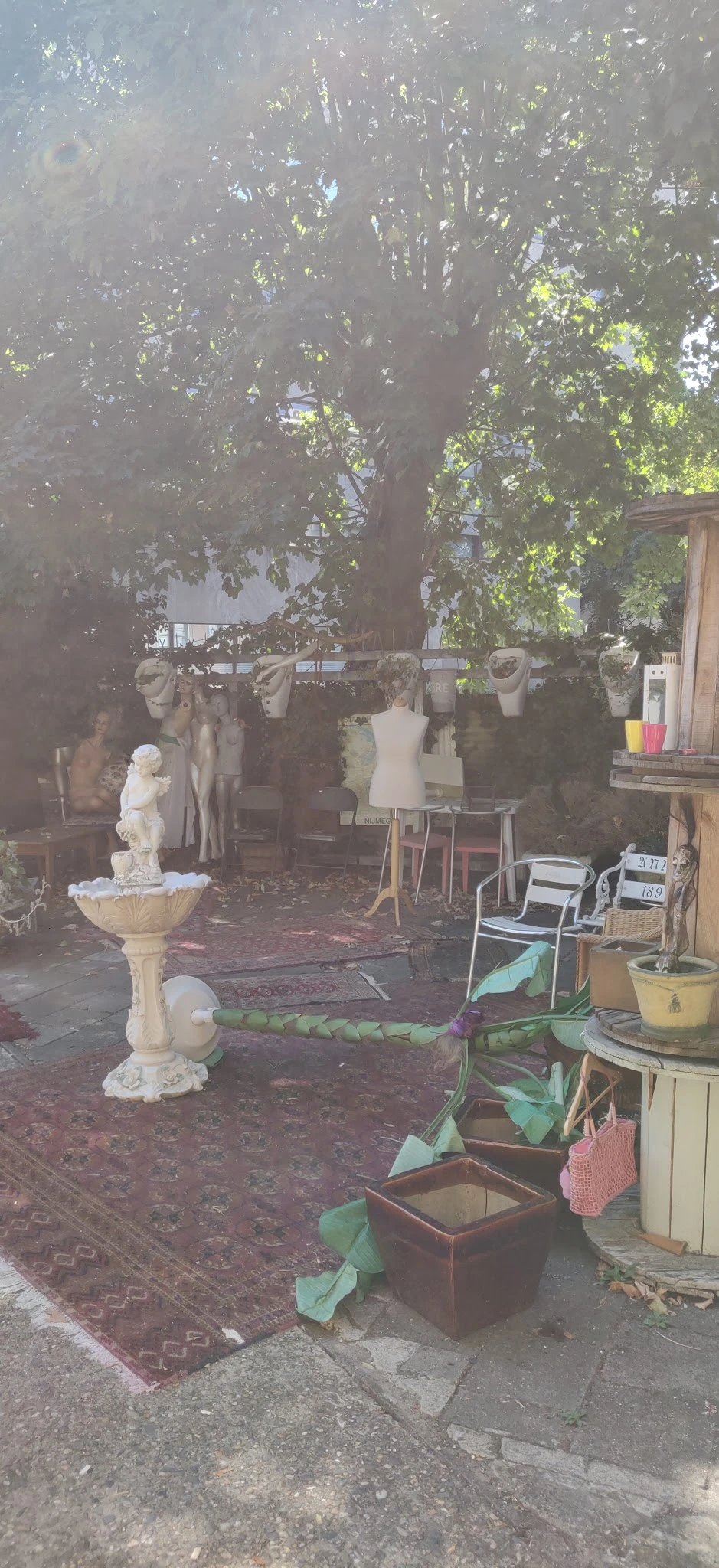 Winkelinterieur met mannequins, kleding aan rekken, bankje en decoratieve objecten zoals een vogelbadje en planten
