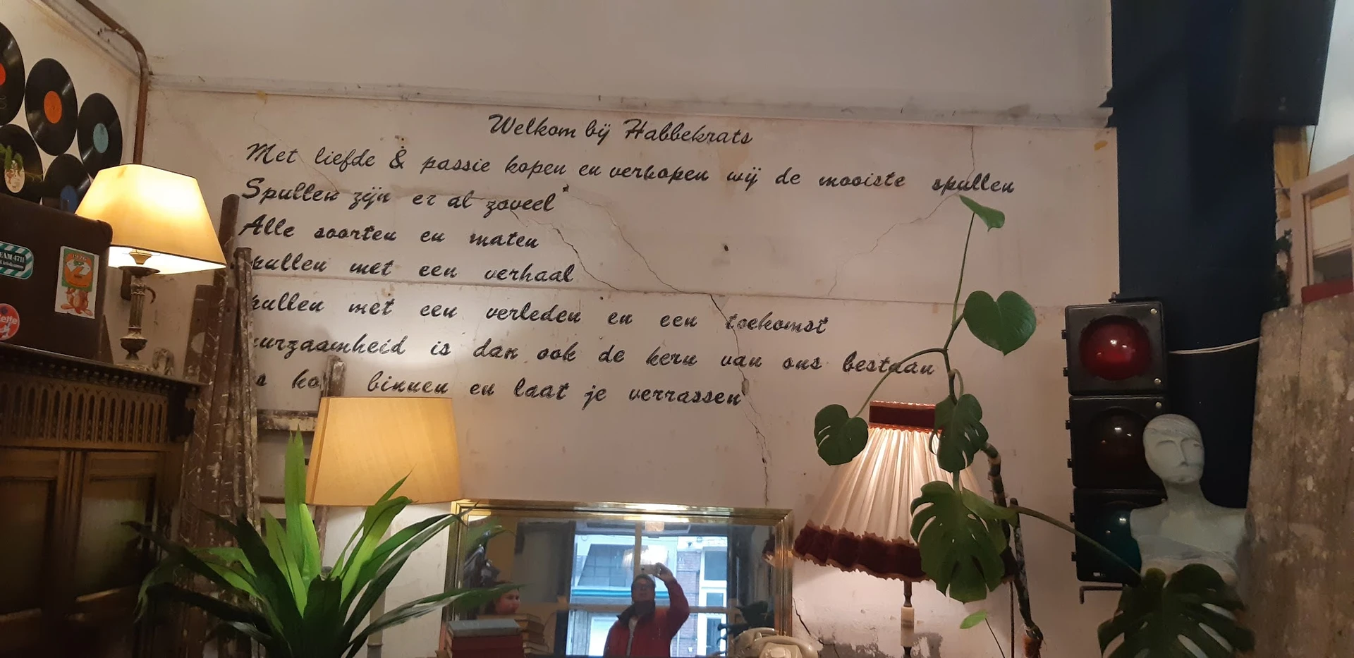 Interieurfoto met muurtekst 'Welkom bij Habbekrats', lamp, plant en raam
