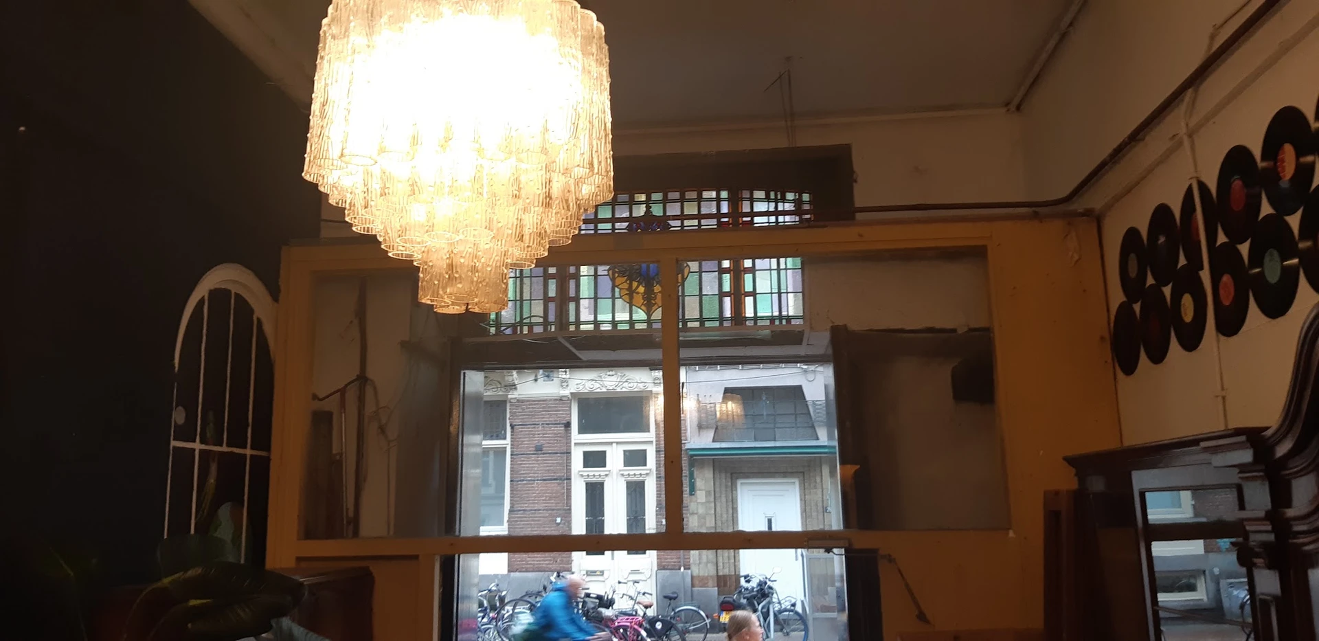 Winkelbinnenkant met glazen voorzijde, moderne hanglamp, houten balustrade en zicht naar straat met voorbijgangers