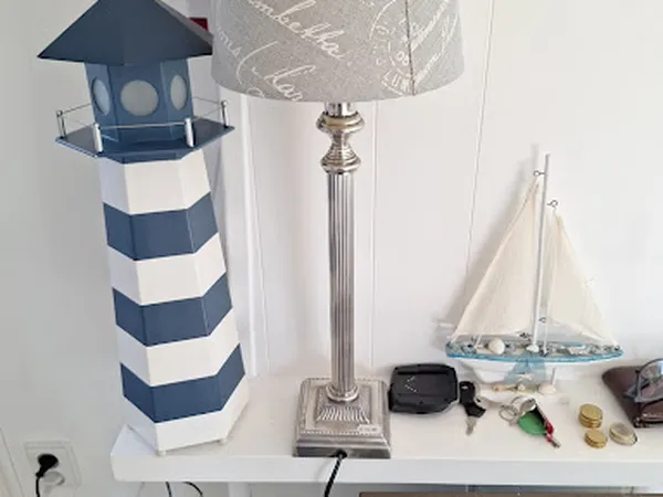 Uitgestalde decoratieve artikelen: een gestreepte vuurtoren, staande lamp, zeilboot en overige accessoires op een witte plank