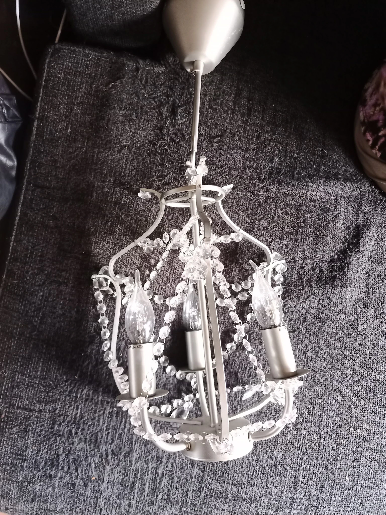 Witte kroonluchter met kristallen hangers en metalen fitting tegen grijze achtergrond