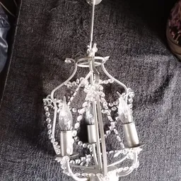 Witte kroonluchter met kristallen hangers en metalen fitting tegen grijze achtergrond