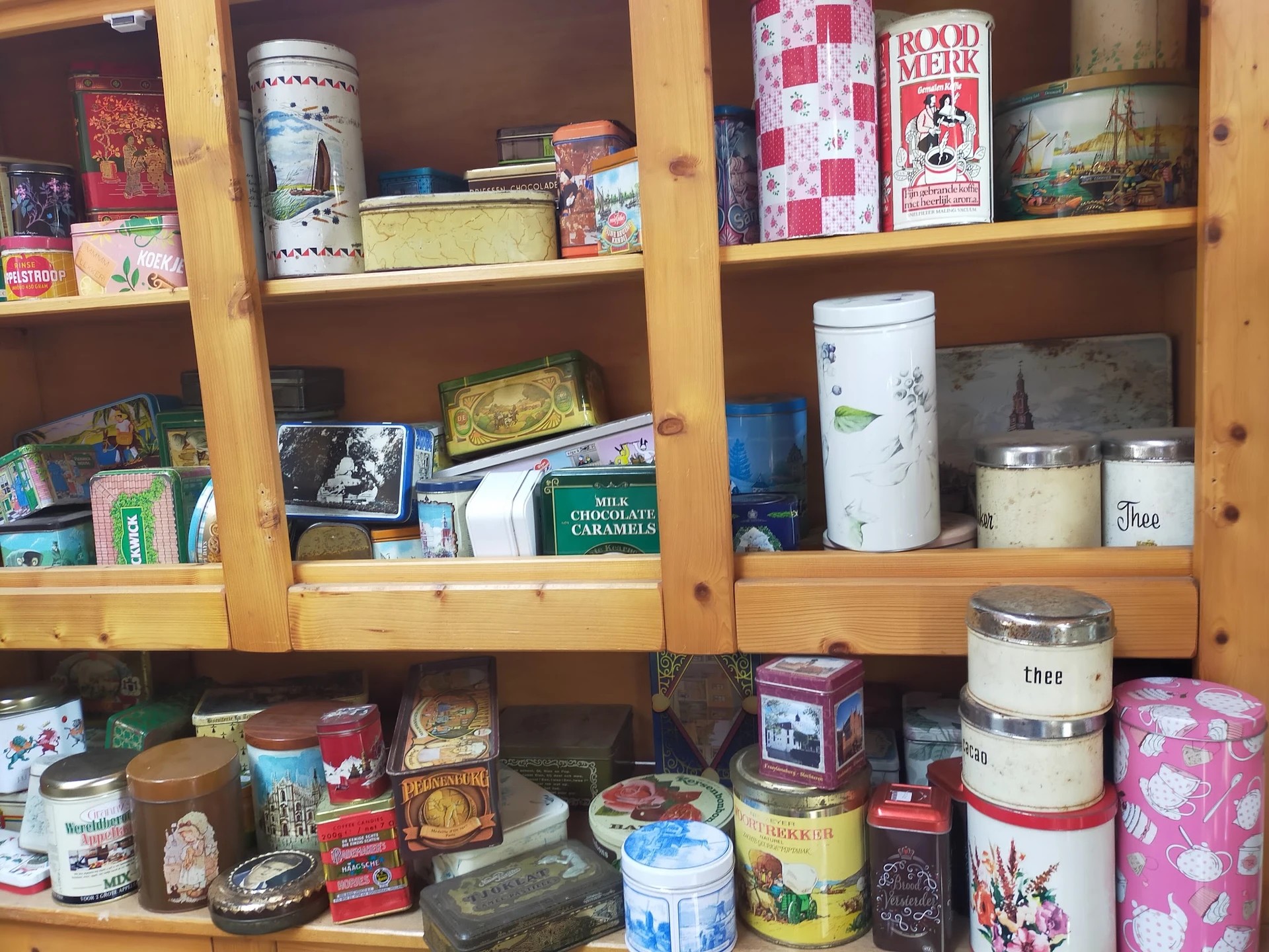 Houten vitrinekast met diverse vintage blikken, potjes en decoratieve items uit de winkelcollectie