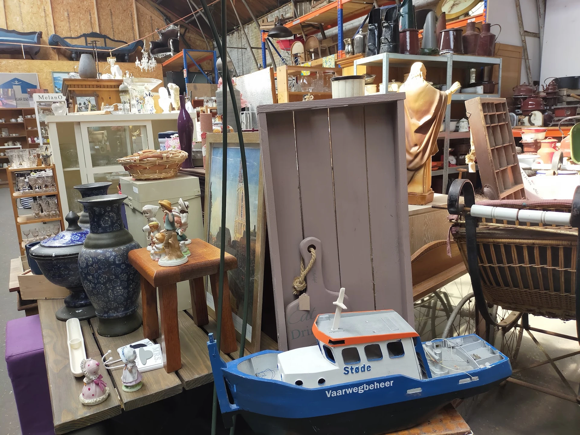 Diverse gebruikte huishoudartikelen en meubelstukken in een kringloopwinkel, waaronder een speelgoedboot, tafel en kasten