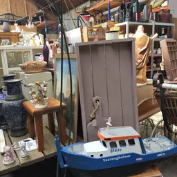 Diverse gebruikte huishoudartikelen en meubelstukken in een kringloopwinkel, waaronder een speelgoedboot, tafel en kasten