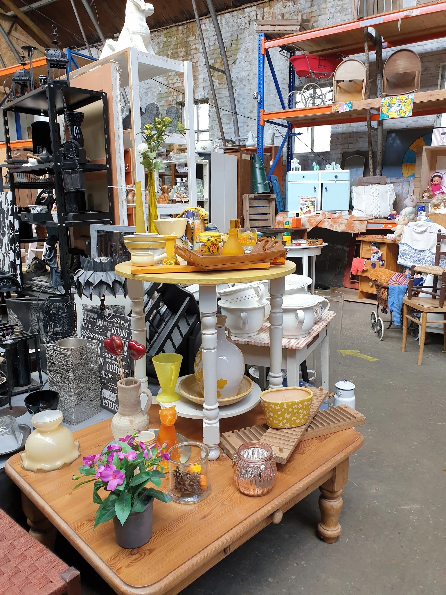 Huishoudelijke spullen en decoratie uitgestald op een tafel: serviesgoed, keukengerei, plantenpotten en houten accessoires