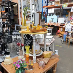 Huishoudelijke spullen en decoratie uitgestald op een tafel: serviesgoed, keukengerei, plantenpotten en houten accessoires