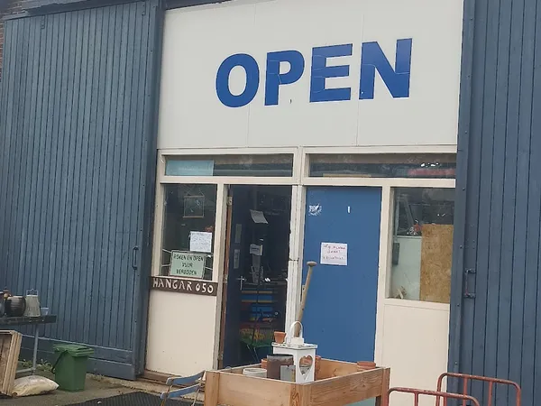 Winkelpui met blauw OPEN-bord, blauwe deur en witte zijpanelen, enkele obstakels op de stoep