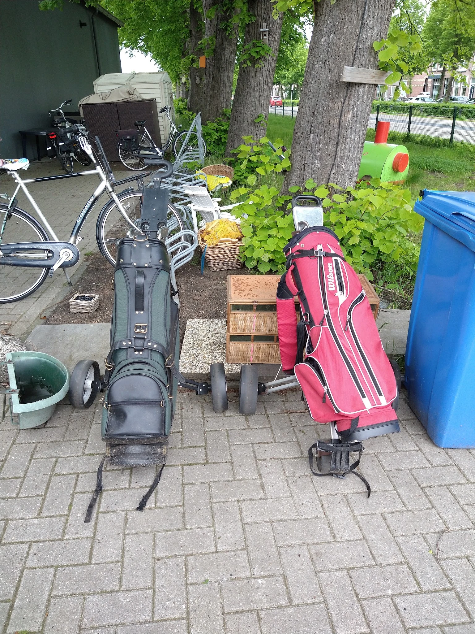 Tweedehands golfbags en sporttassen uitgestald op een patio naast fietsen en tuinartikelen