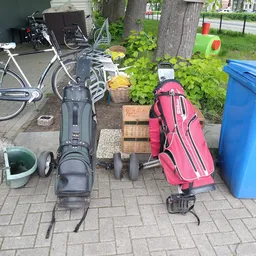 Tweedehands golfbags en sporttassen uitgestald op een patio naast fietsen en tuinartikelen