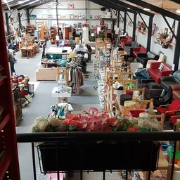 Overzicht van kringloophal met uitgestalde meubels, rekken met spullen en rode fauteuils aan de rechterkant