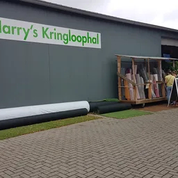 Grijze gevel van Harry's Kringloophal met groen logo, voorzijde met houten materialen en bouwmateriaal op stapel voor de inga