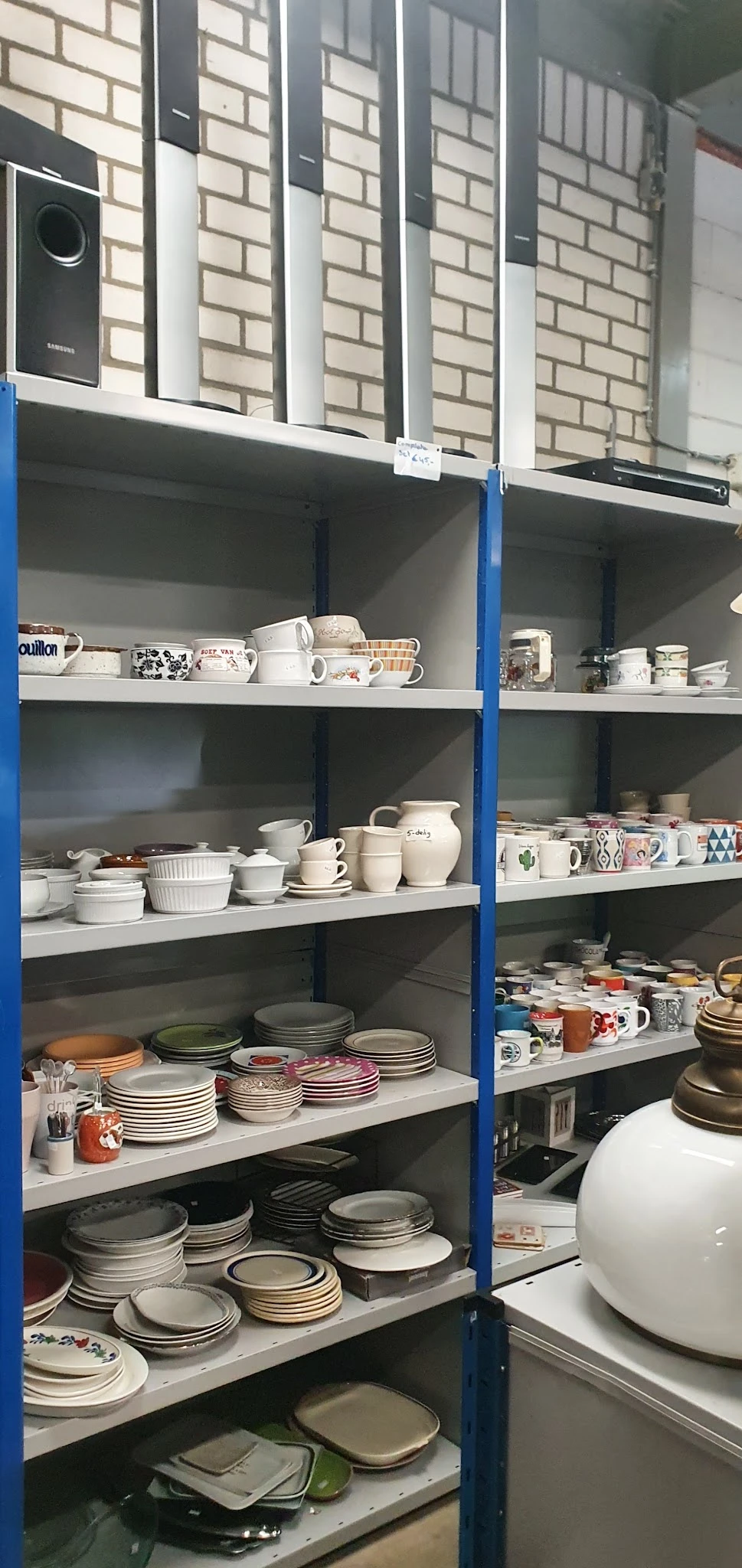 Blauw stellingkast met witte keramische servies, kopjes, kannen en borden netjes uitgestald op vier niveaus