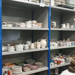 Blauw stellingkast met witte keramische servies, kopjes, kannen en borden netjes uitgestald op vier niveaus
