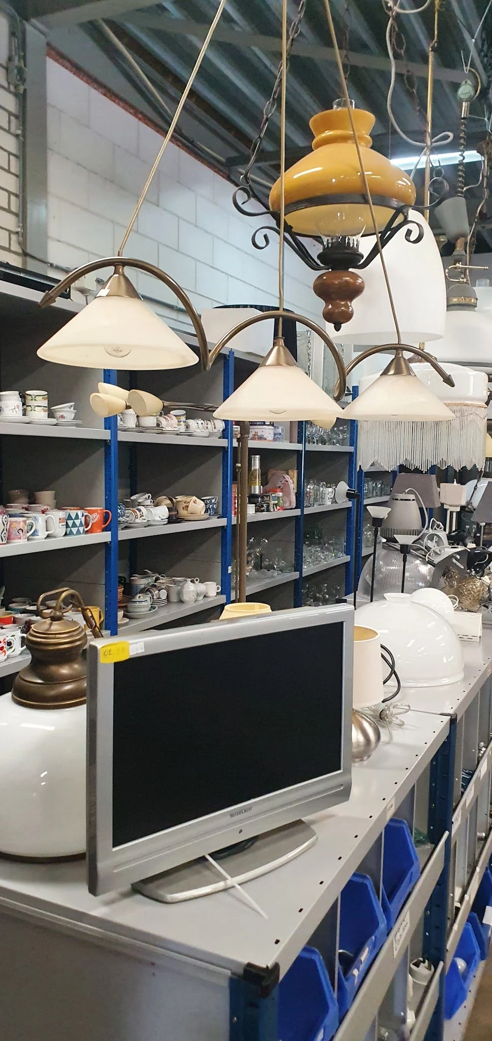 Stellingen vol serviesgoed, glazen en huishoudartikelen in een kringloopwinkel