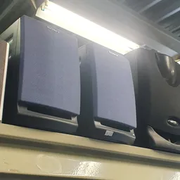 Drie zwarte Sony luidsprekers op een plank tegen een witte muur