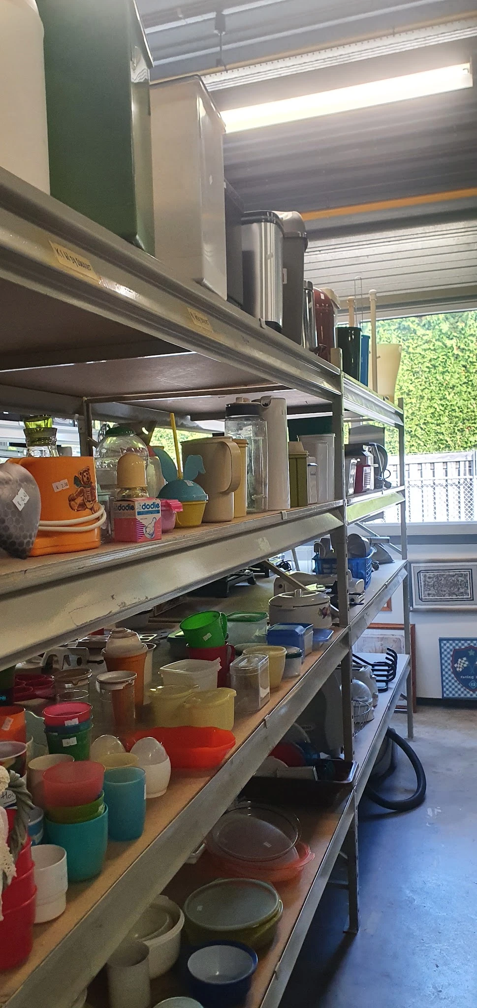 Metalen stellingen met diverse huishoudelijke artikelen en decoratiespullen, waaronder dozen, tassen en aardewerk
