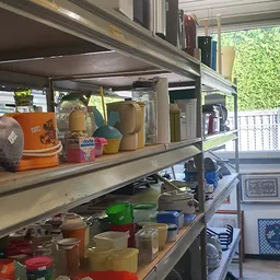 Metalen stellingen met diverse huishoudelijke artikelen en decoratiespullen, waaronder dozen, tassen en aardewerk