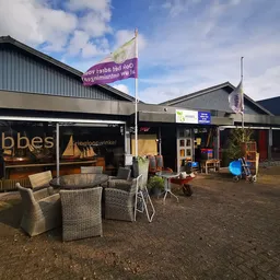 Voorkant van kringloopwinkel Hebbes met naam op raam, terras met stoelen en personeel in deuropening
