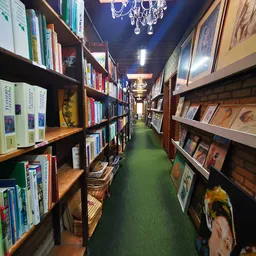Winkelgang met boekenrekken aan weerszijden en groen tapijt, kunstwerken aan de muren
