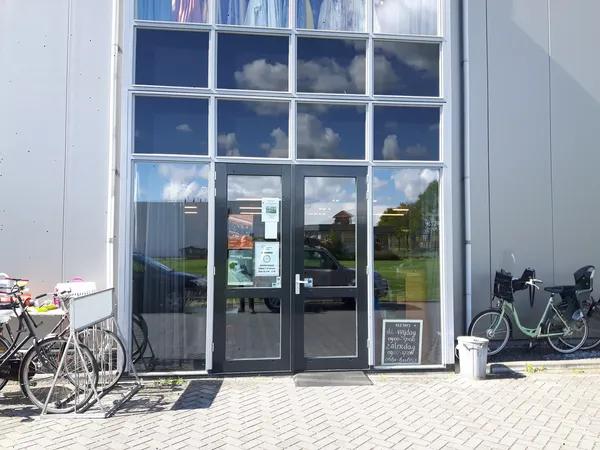 Voorkant van kringloopwinkel met glazen deuren en ramen, fietsen op de stoep