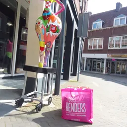 Straatfront van kringloopwinkel met kleurrijke decoratie en roze tas op straat