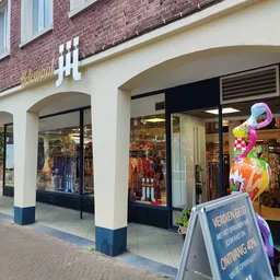 Winkelgevel van kringloopwinkel met witte en bruine gevelsteen, zwarte winkeldeuren en ramen met kleding en spullen in de eta