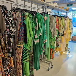 Rekken met kleurrijke tweedehands dameskleding, vooral groene en gele kledingstukken.