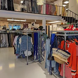 Rekken met tweedehands kleding, waaronder blouses, jurken en rode items, in een kringloopwinkel
