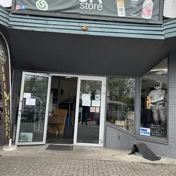 Voorgevel van kringloopwinkel met glazen deuren en etalages, onderkant van uithangbord zichtbaar