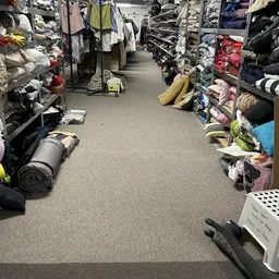 Winkelgang met stellingen vol kleding, schoenen en huishoudspullen aan beide zijden