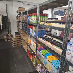 Winkelgang met metalen stellingen vol huishoudproducten, schoonmaakmiddelen en textiel, links kleding aan rekken