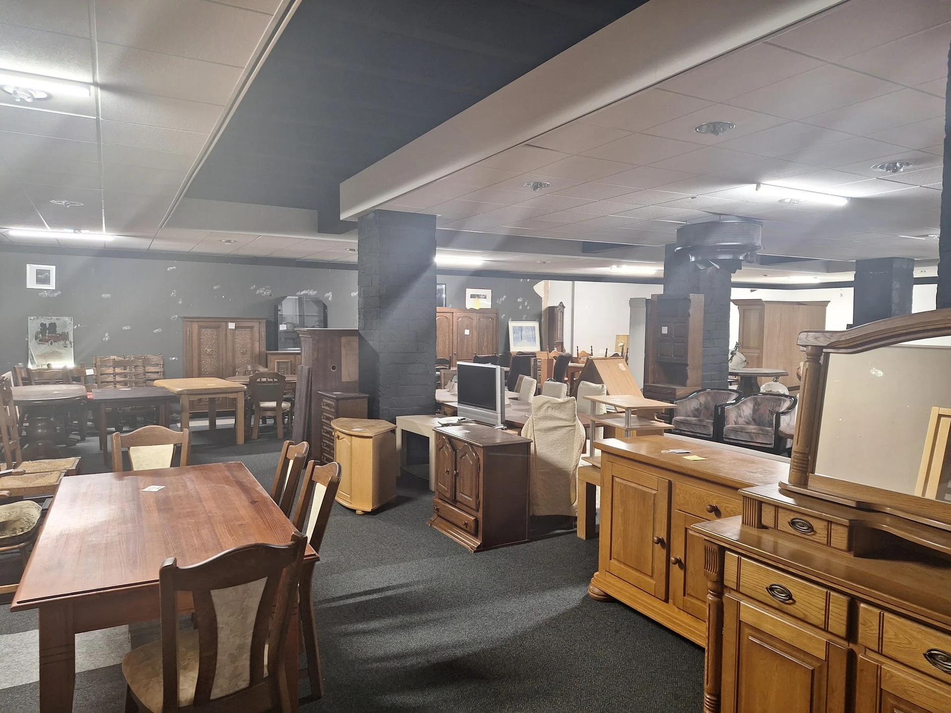 Ruim interieur van kringloopwinkel met diverse meubels, tafels, kasten en huishoudelijke artikelen uitgestald