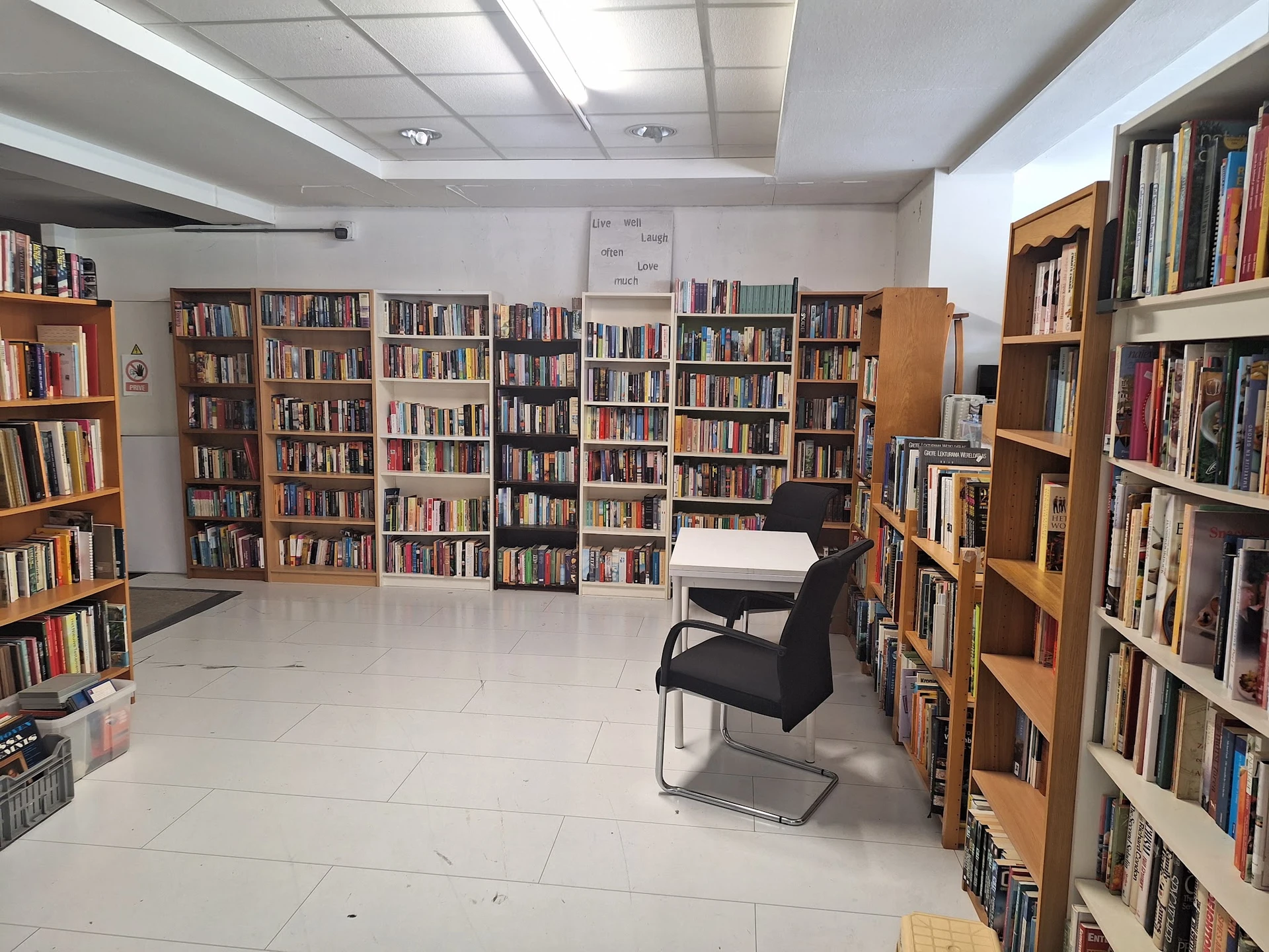 Boekenrekken langs de wanden van een ruime kringloopwinkel met een lichte vloer en zitgelegenheid