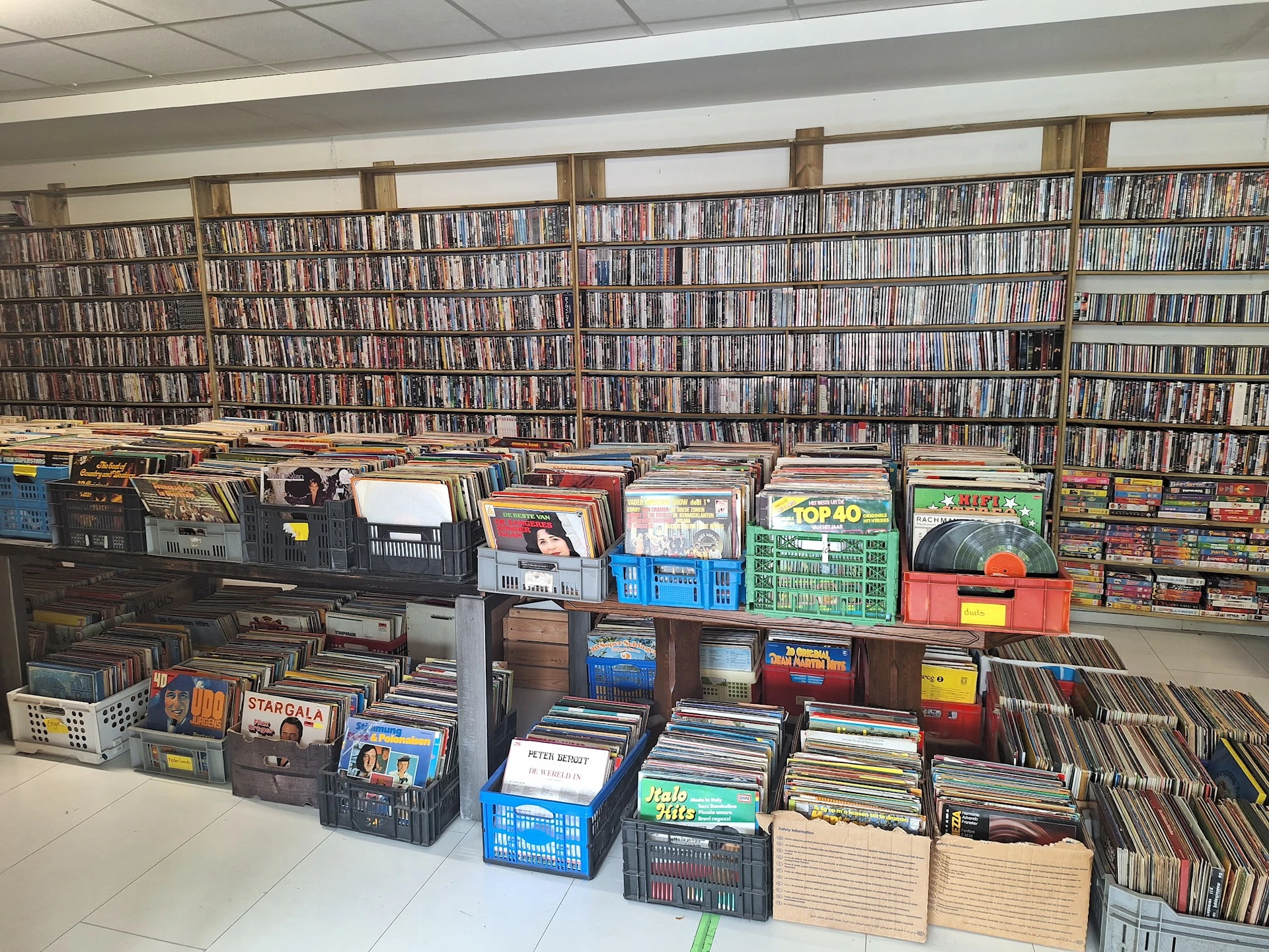 Uitgestalde cd's, dvd's en vinyl records in dozen en kratten in de winkel, met volle cd-kasten op de achtergrond