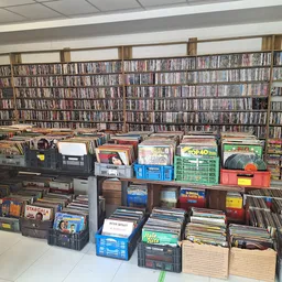 Uitgestalde cd's, dvd's en vinyl records in dozen en kratten in de winkel, met volle cd-kasten op de achtergrond