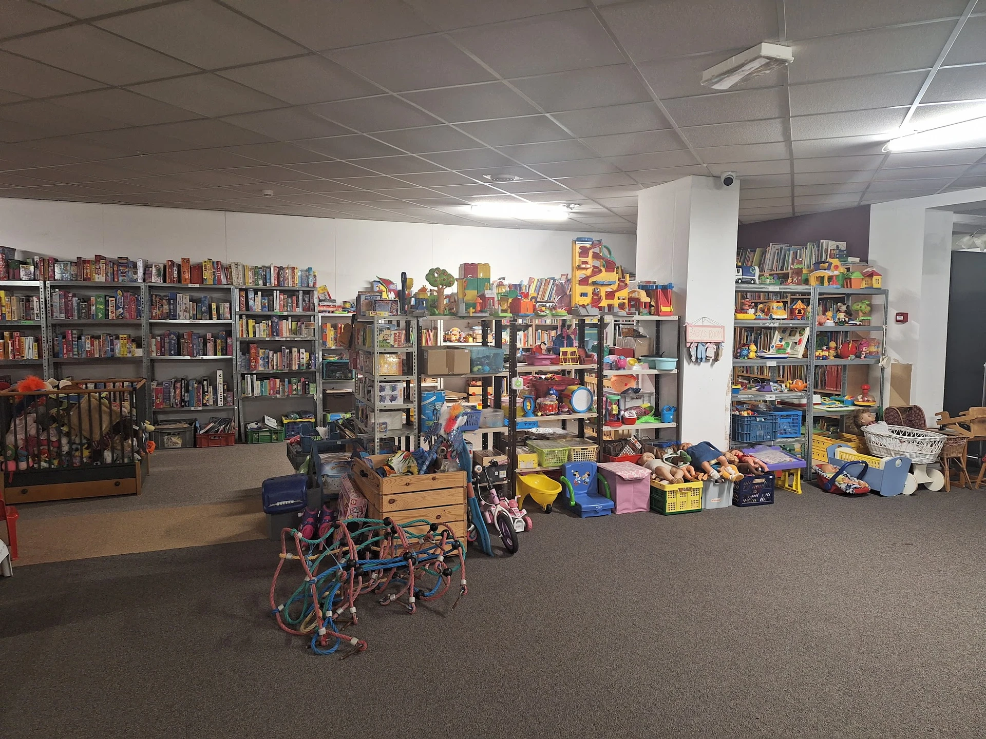 Winkelvloer met boekenkasten, speelgoed, kinderartikelen en diverse spullen in containers en op stellingen
