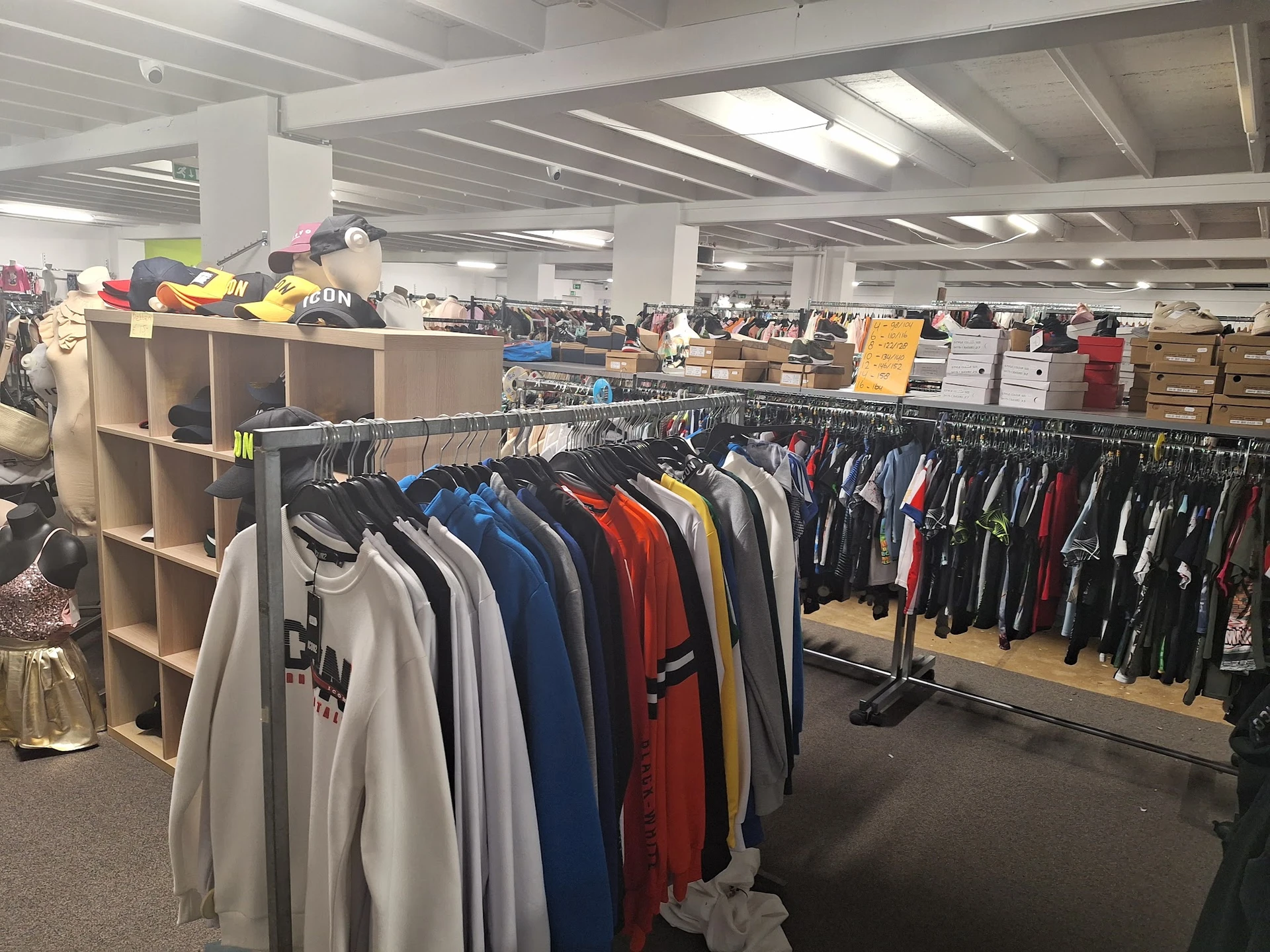 Winkelinterieur met kledingrekken vol tweedehands kleding, stellages en dozen op het dak, fluorescente verlichting