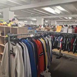 Winkelinterieur met kledingrekken vol tweedehands kleding, stellages en dozen op het dak, fluorescente verlichting