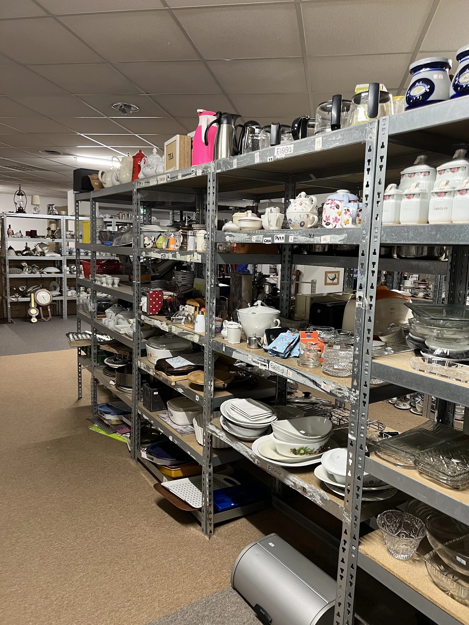 Metalen stellingen met serviesgoed, borden, schalen en keukengerei in een kringloopwinkel