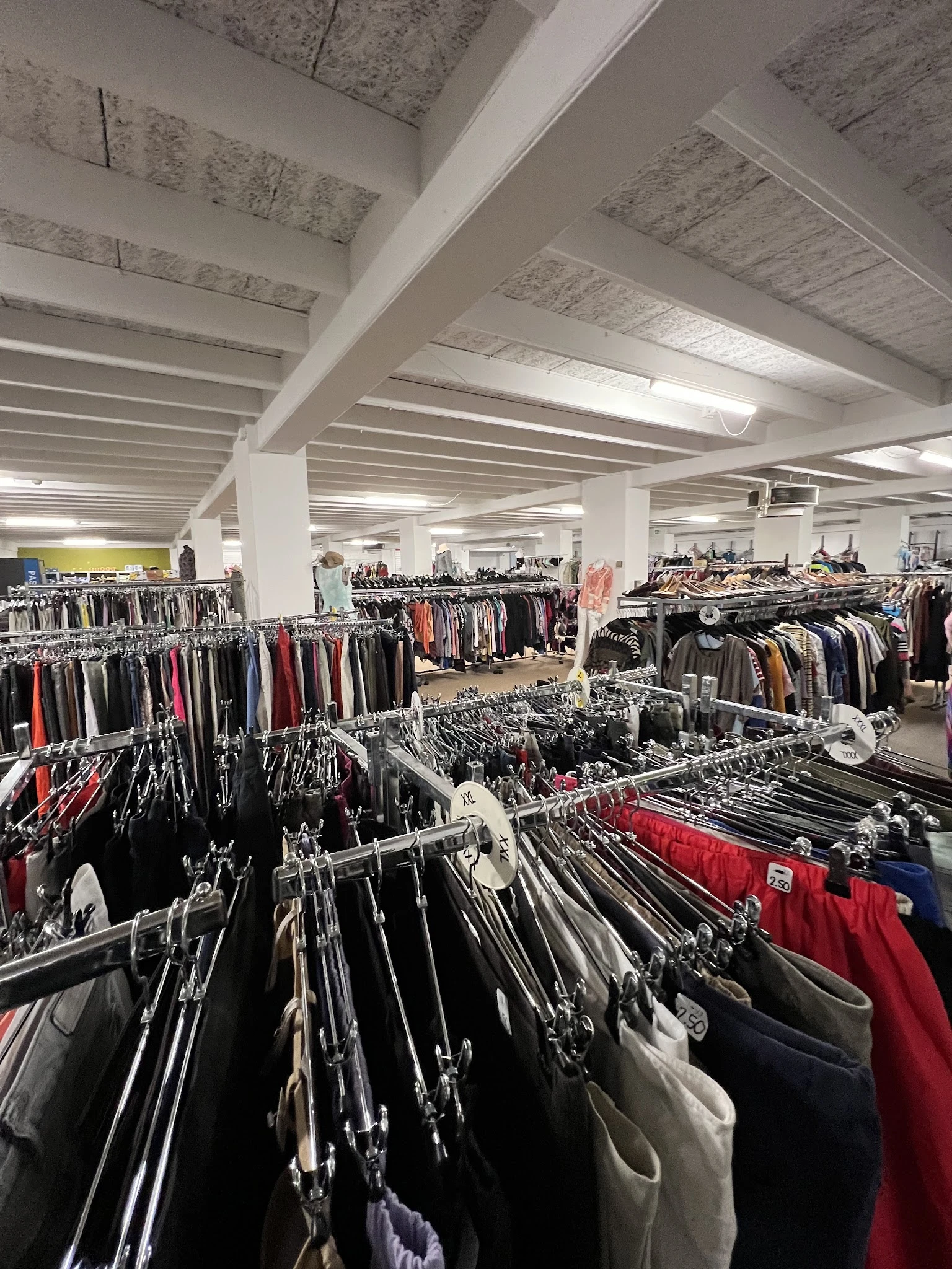 Uitgebreide rekken met tweedehands kleding in verschillende kleuren in een ruime winkelhal met witte kolommen