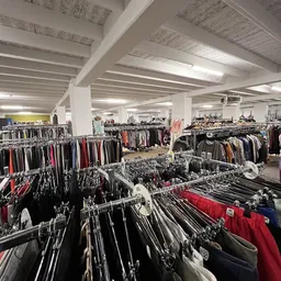Uitgebreide rekken met tweedehands kleding in verschillende kleuren in een ruime winkelhal met witte kolommen