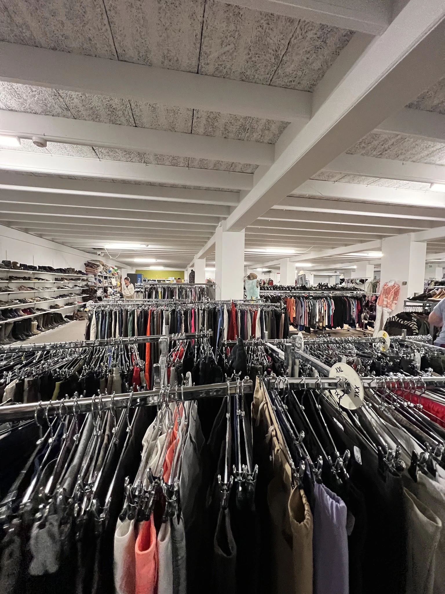 Overzicht van rekken met tweedehands kleding op hangers in een grote winkelruimte