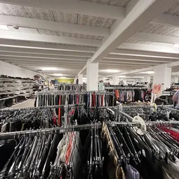 Overzicht van rekken met tweedehands kleding op hangers in een grote winkelruimte